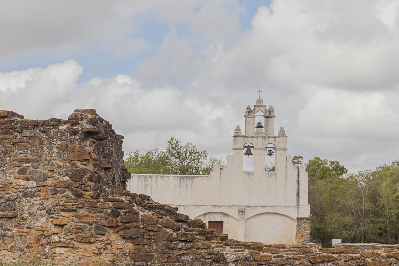 White frescoed church with a stone ruin to the left in the foreground. 