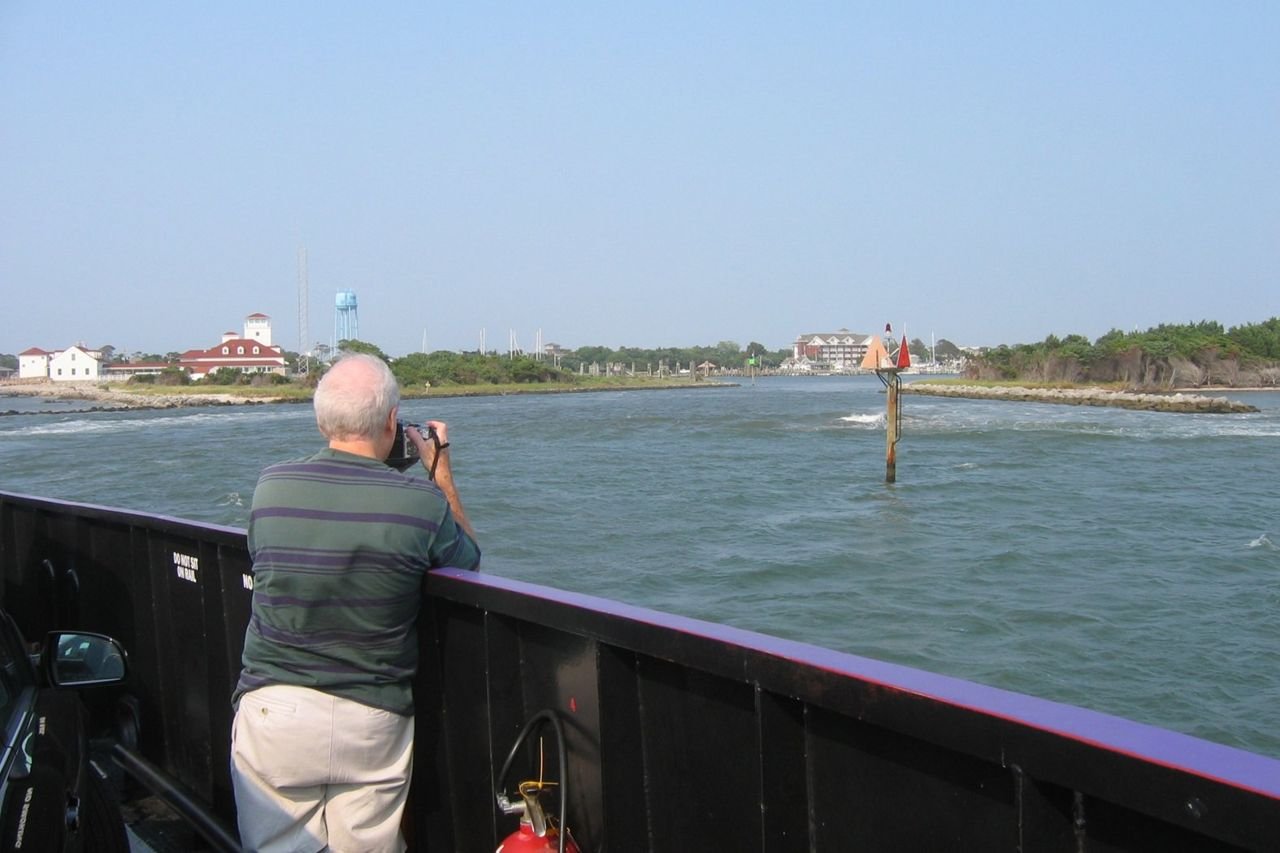 A summer visitor to the Outer Banks Scenic Byway engages in a favorite pastime on the ferry leaving Ocracoke’s Silver Lake, photographing the harbor and the enormous former U.S. Coast Guard Station, built in 1935.