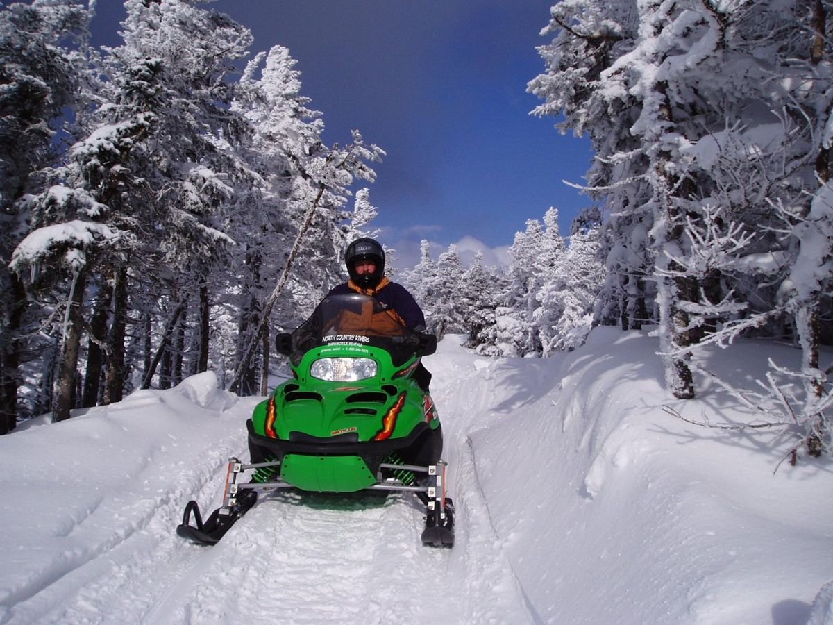 A rider in a bright green sled takes to a narrow trail near Rangeley Lakes Scenic Byway.