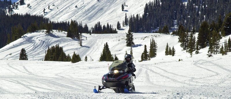 Powder flies as a snowmobiler takes a turn in the snow at Grand Lake near the Colorado River Headwaters Scenic Byway.