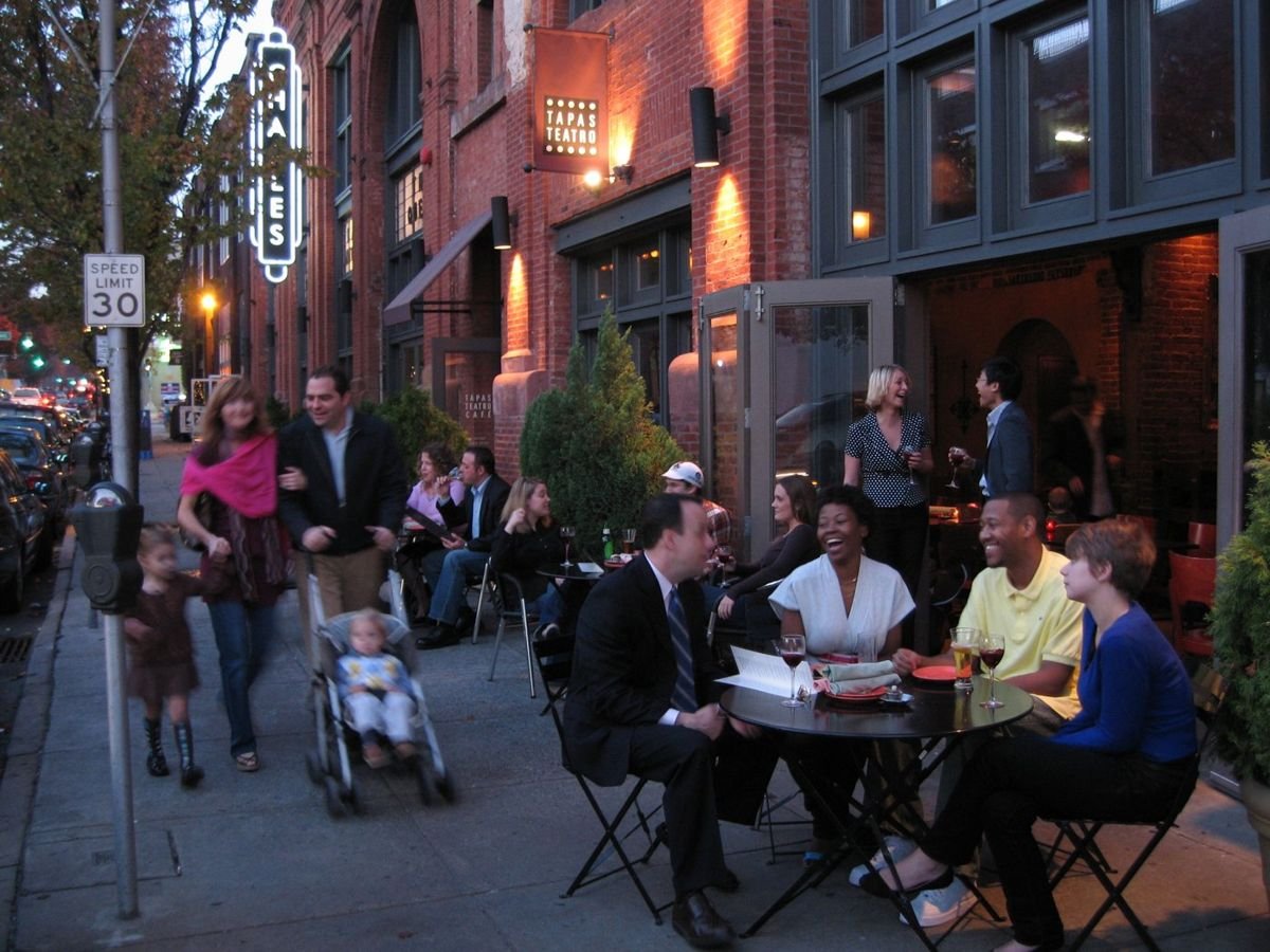 People at tables smile and laugh while a family walks by Baltimore's Station North Arts & Entertainment District, home to the multi-screen Charles Theater.