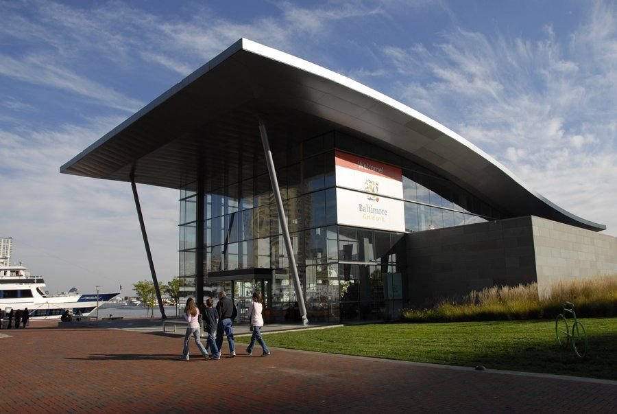 A family strolls past the beautiful metal and glass visitor center at Baltimore’s Inner Harbor, which resembles the water and waves of the Inner Harbor.