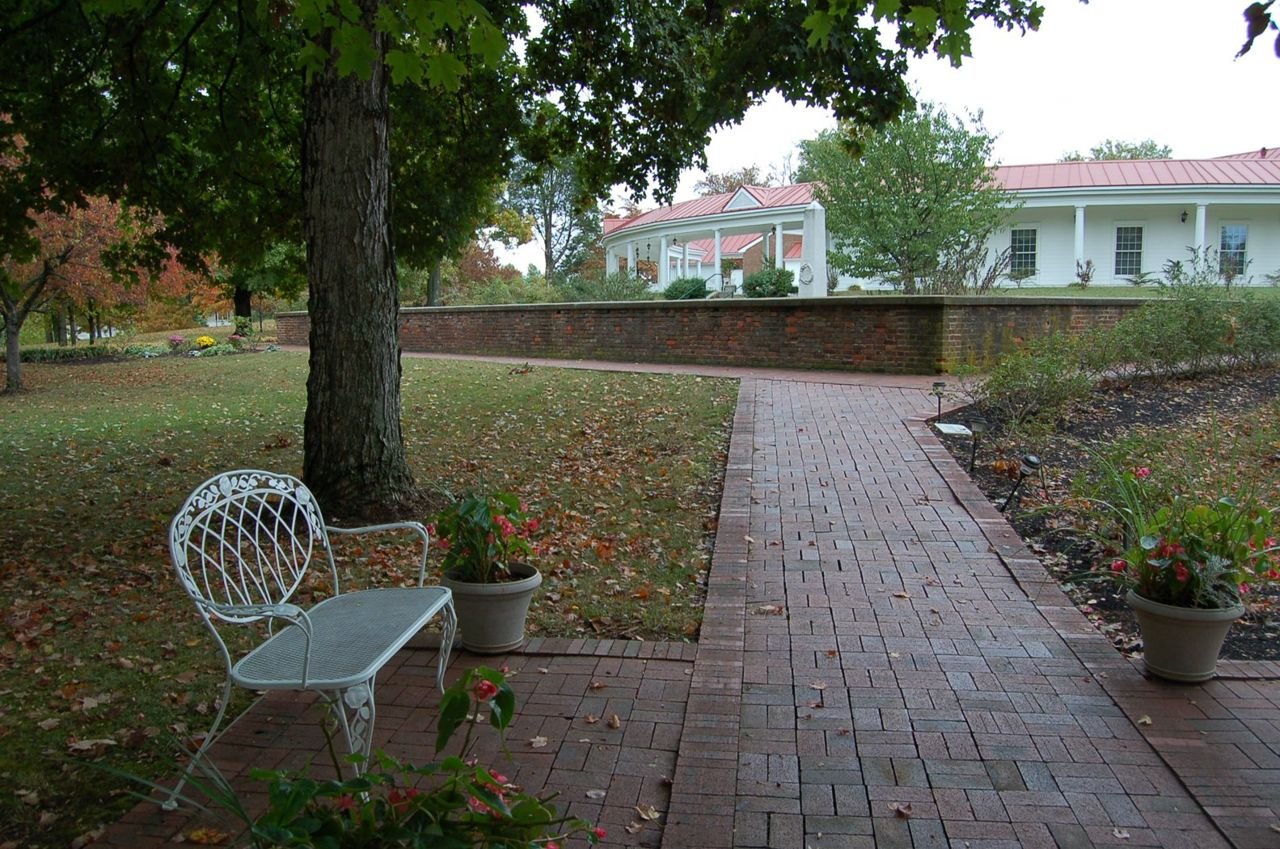 Autumn leaves lie scattered over a bench and path behind the visitor center at My Old Kentucky Home State Park in Bardstown, KY.