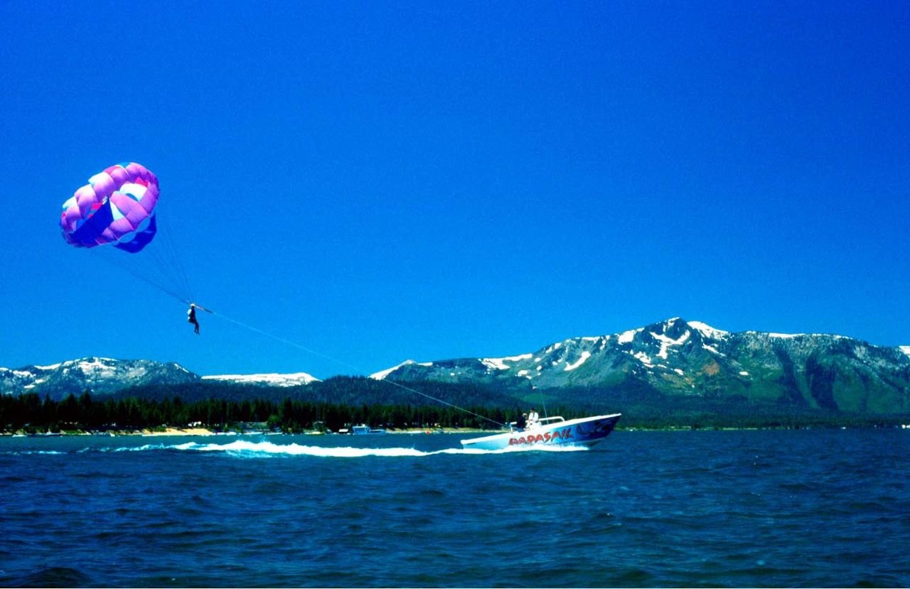 A parasailer rises over the choppy, deep-blue waters of Lake Tahoe behind a speed boat, which provides the sail with lift.