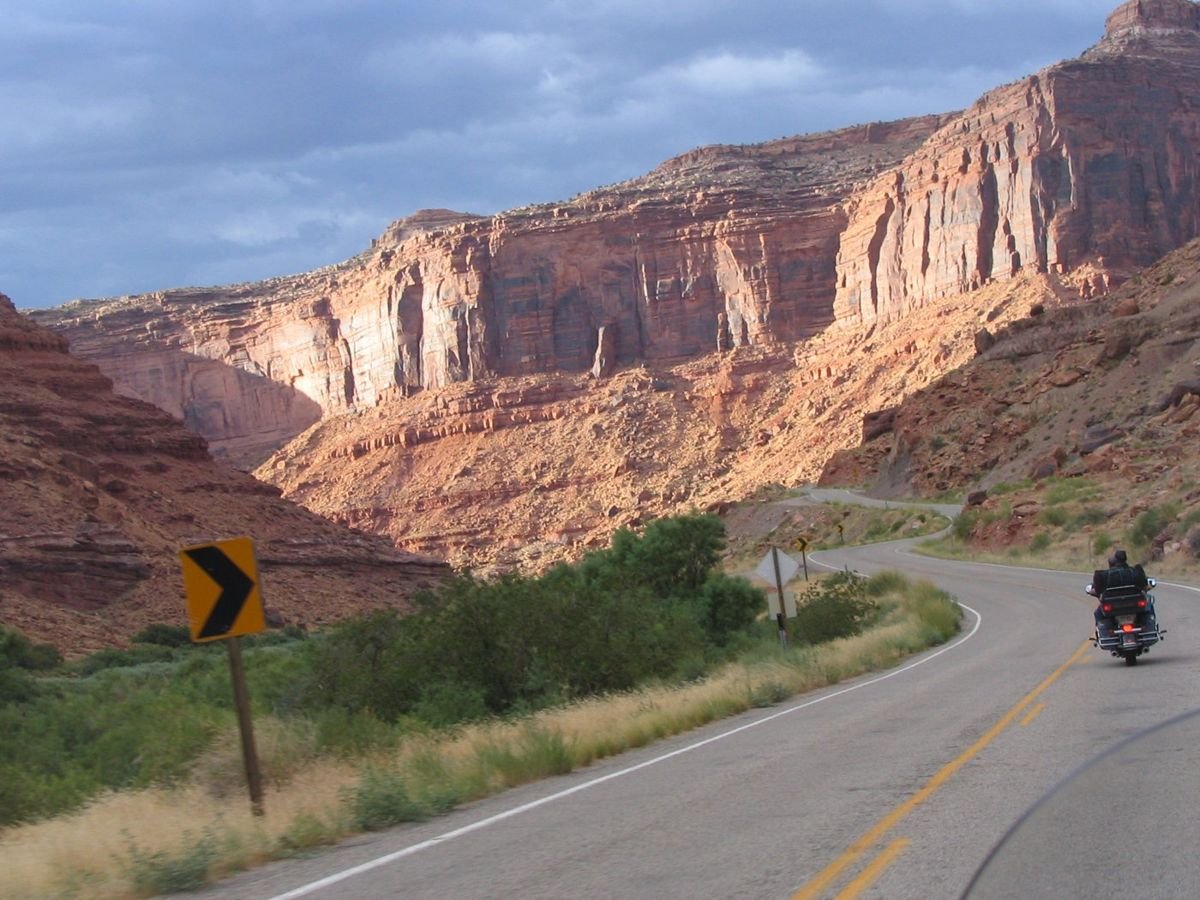 A motorcyclist zooms beneath sunset-lit cliffs on the Colorado River near Moab.