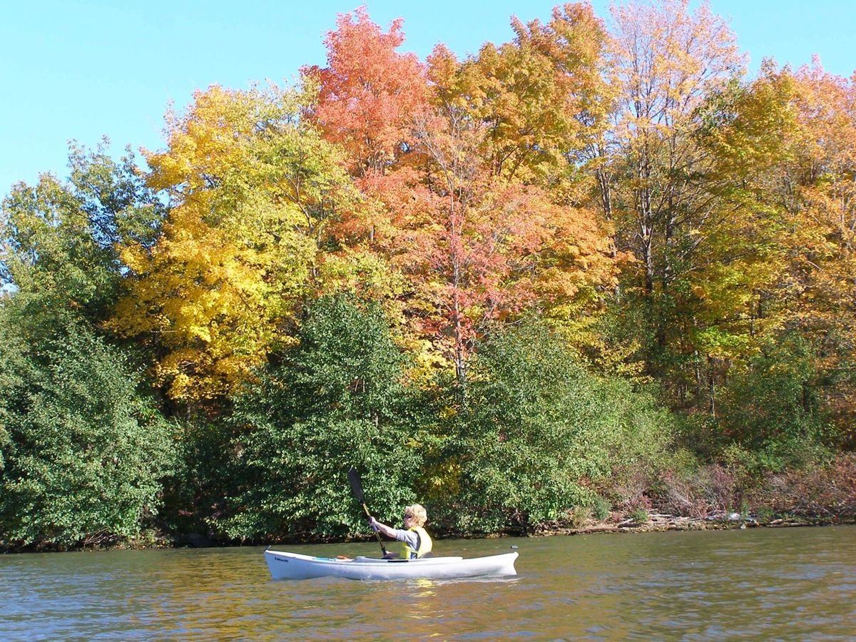 A woman paddles a canoe up the Mohawk River amidst a colorful array of fall foliage.