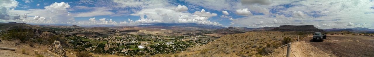 Panorama view of mountains, buildings in a town, and striped mesas with a cloudy sky.