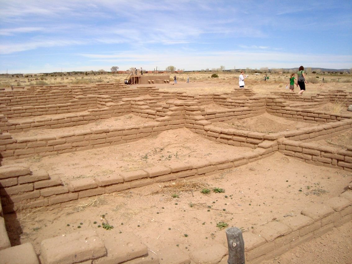 tan-colored pueblo Indian ruins with blue sky and three people